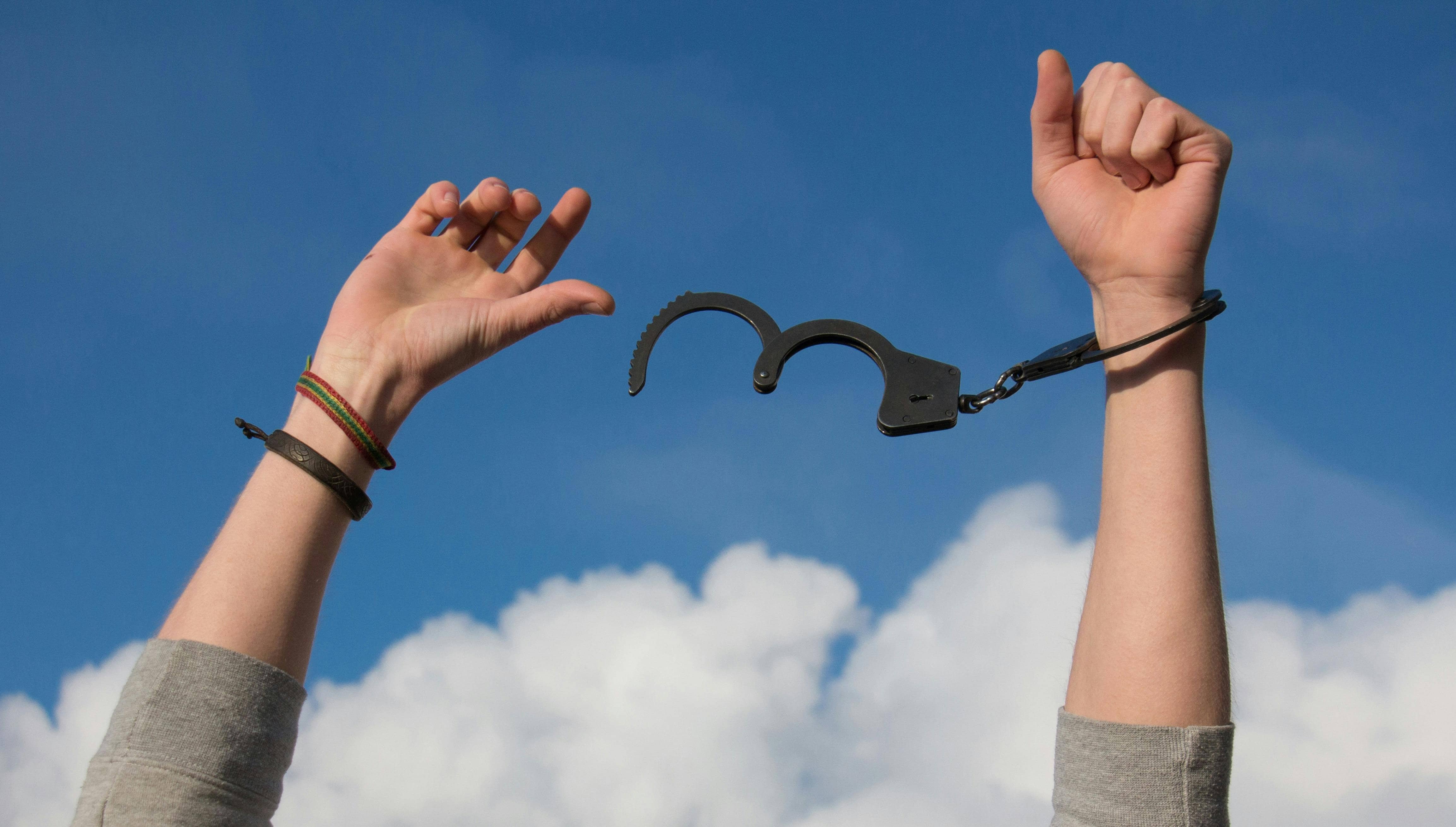 A pair of hands reaching towards the sky, with one wrist still partially cuffed while the other is free, symbolizing liberation.