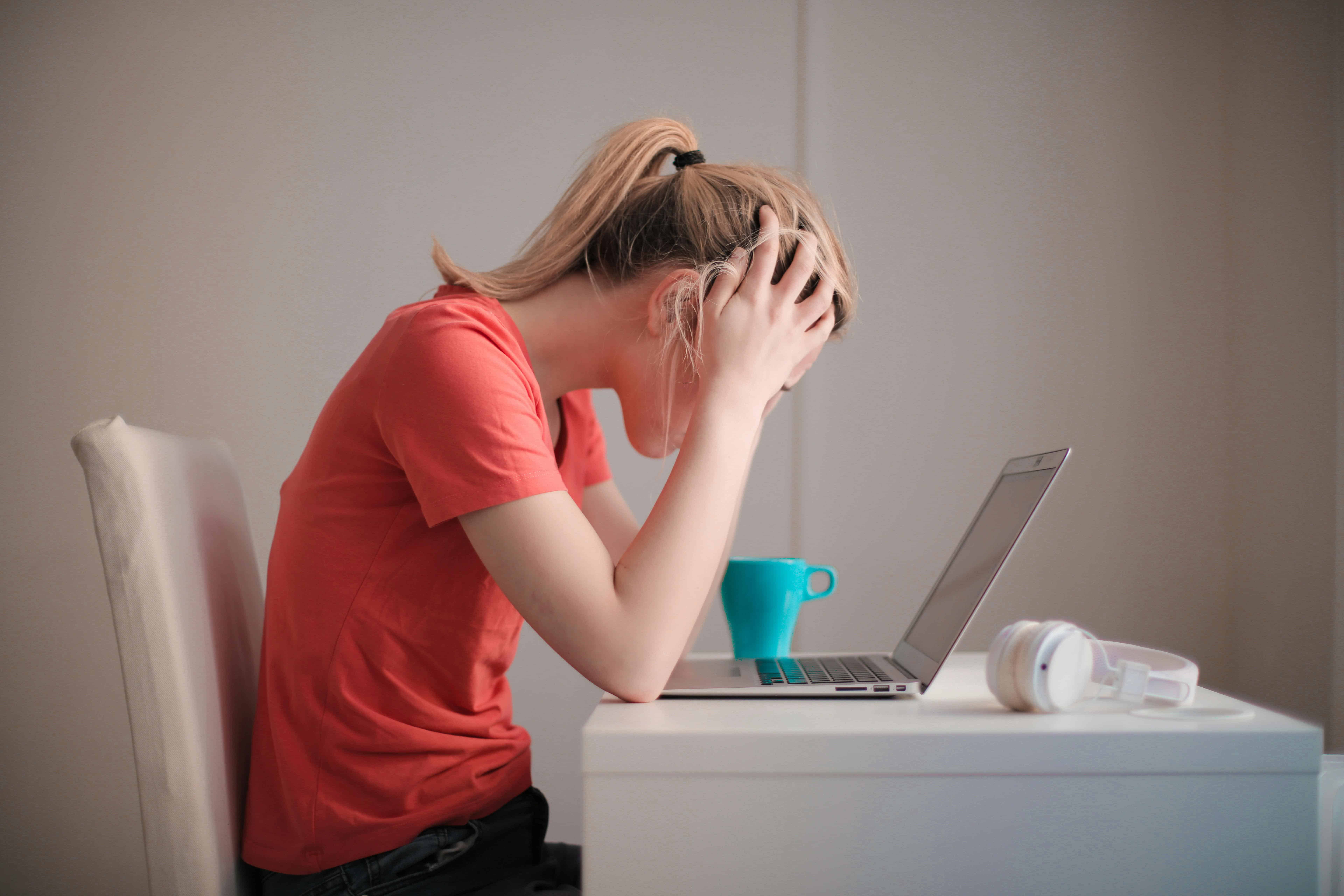 Woman holding her head in frustration while sitting in front of a laptop, symbolizing emotional burnout and stagnation