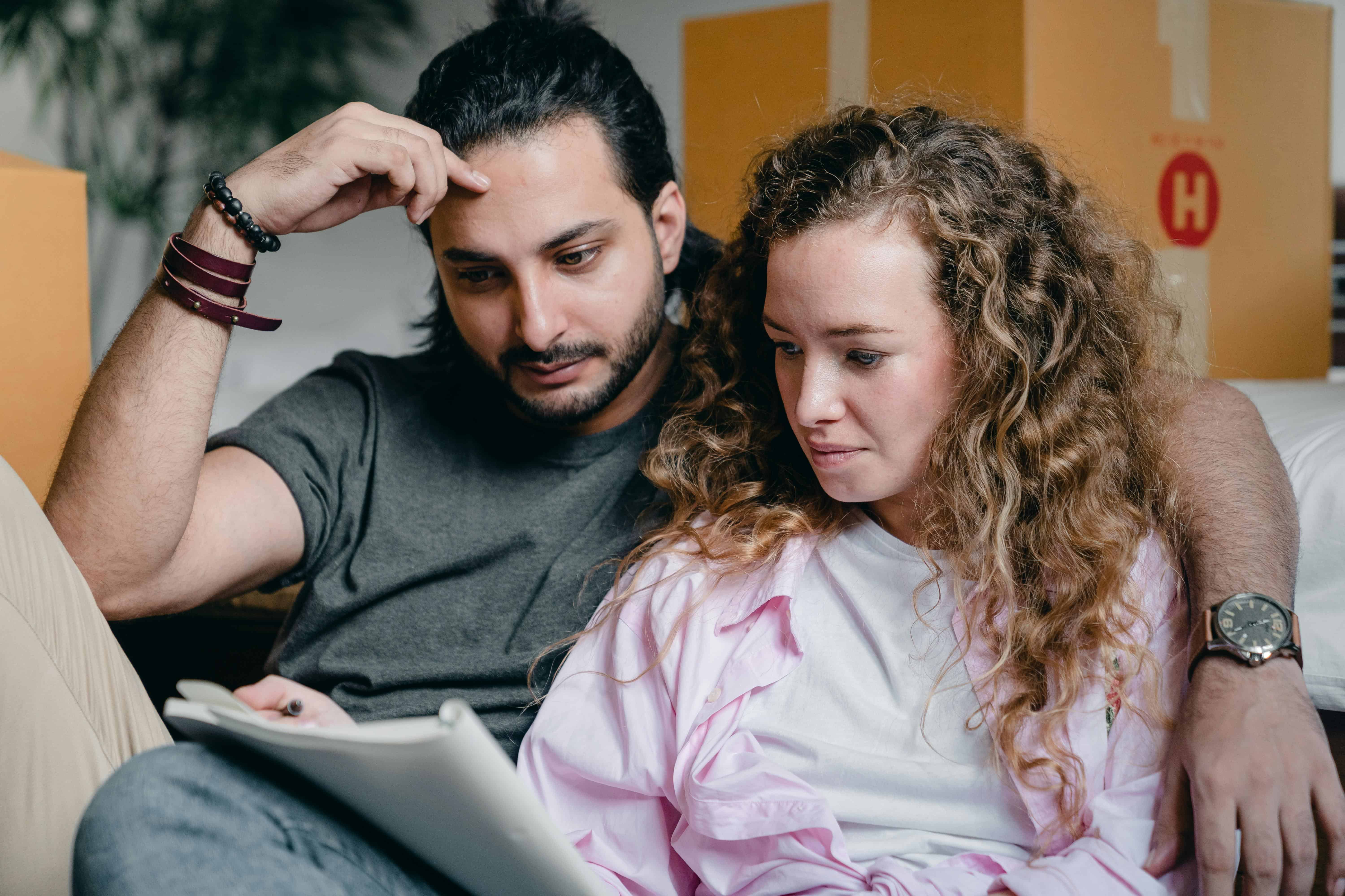 A man and woman sitting close together while reviewing travel documents and plans at home.