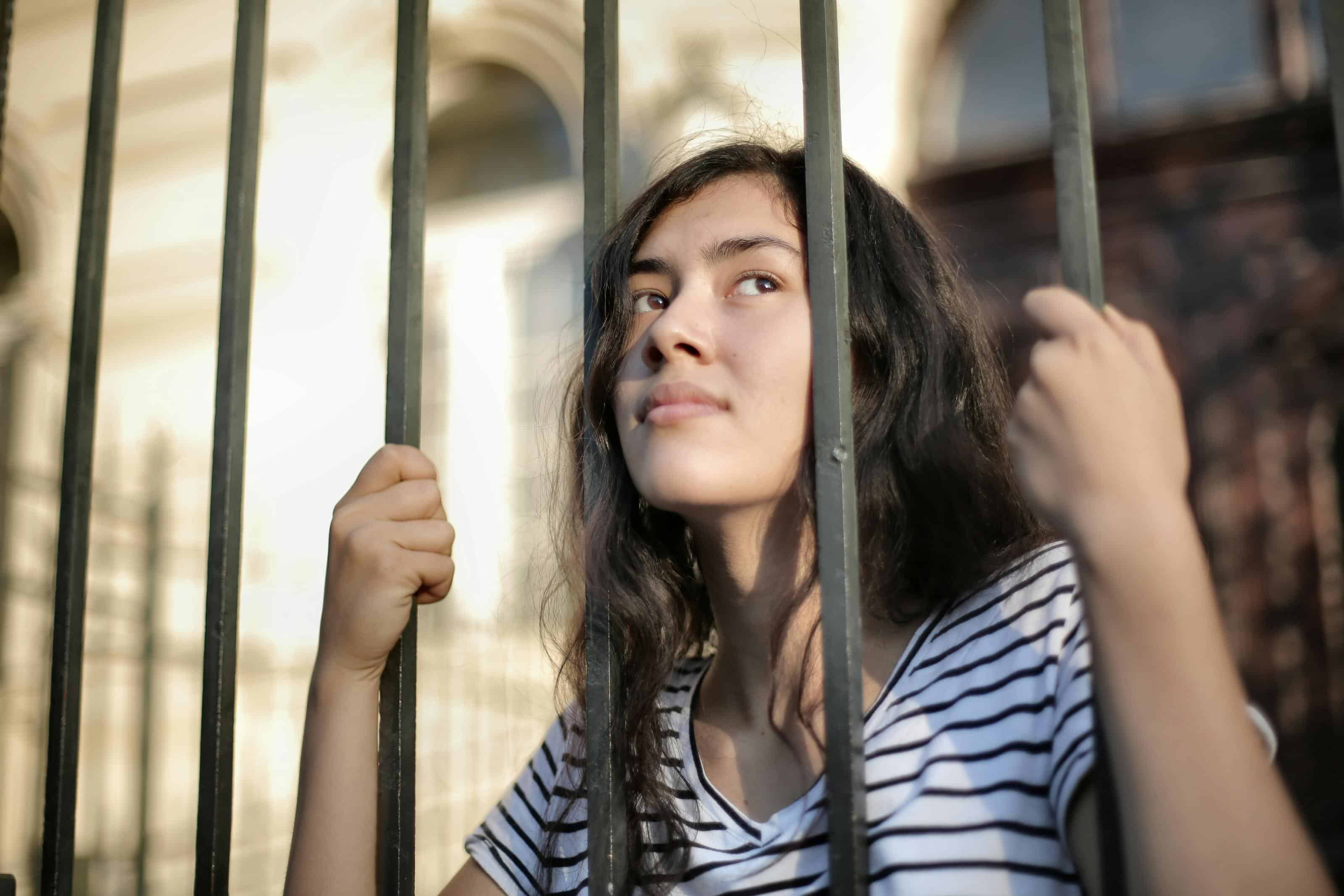 A person holding iron bars while looking upward with a thoughtful expression in soft natural light.