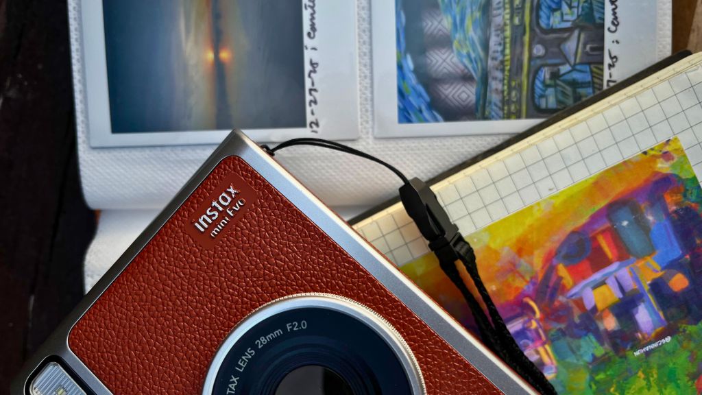 Instax Mini Evo hybrid instant camera resting on a bench beside instant film prints and a notebook