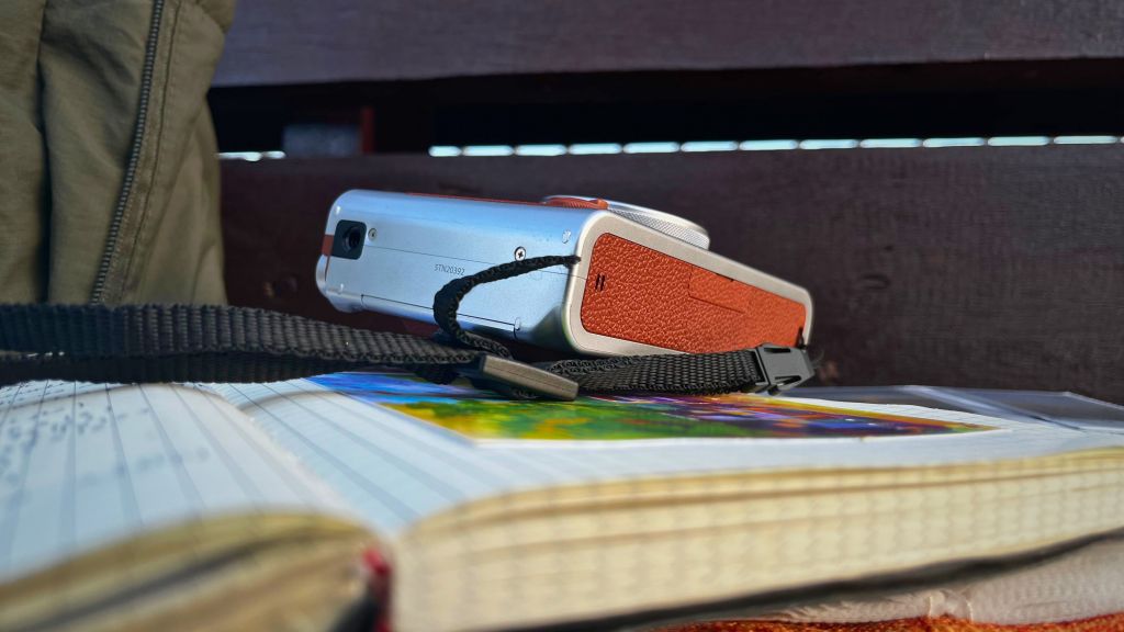 Side view of the Instax Mini Evo hybrid instant camera resting on a notebook on a wooden bench