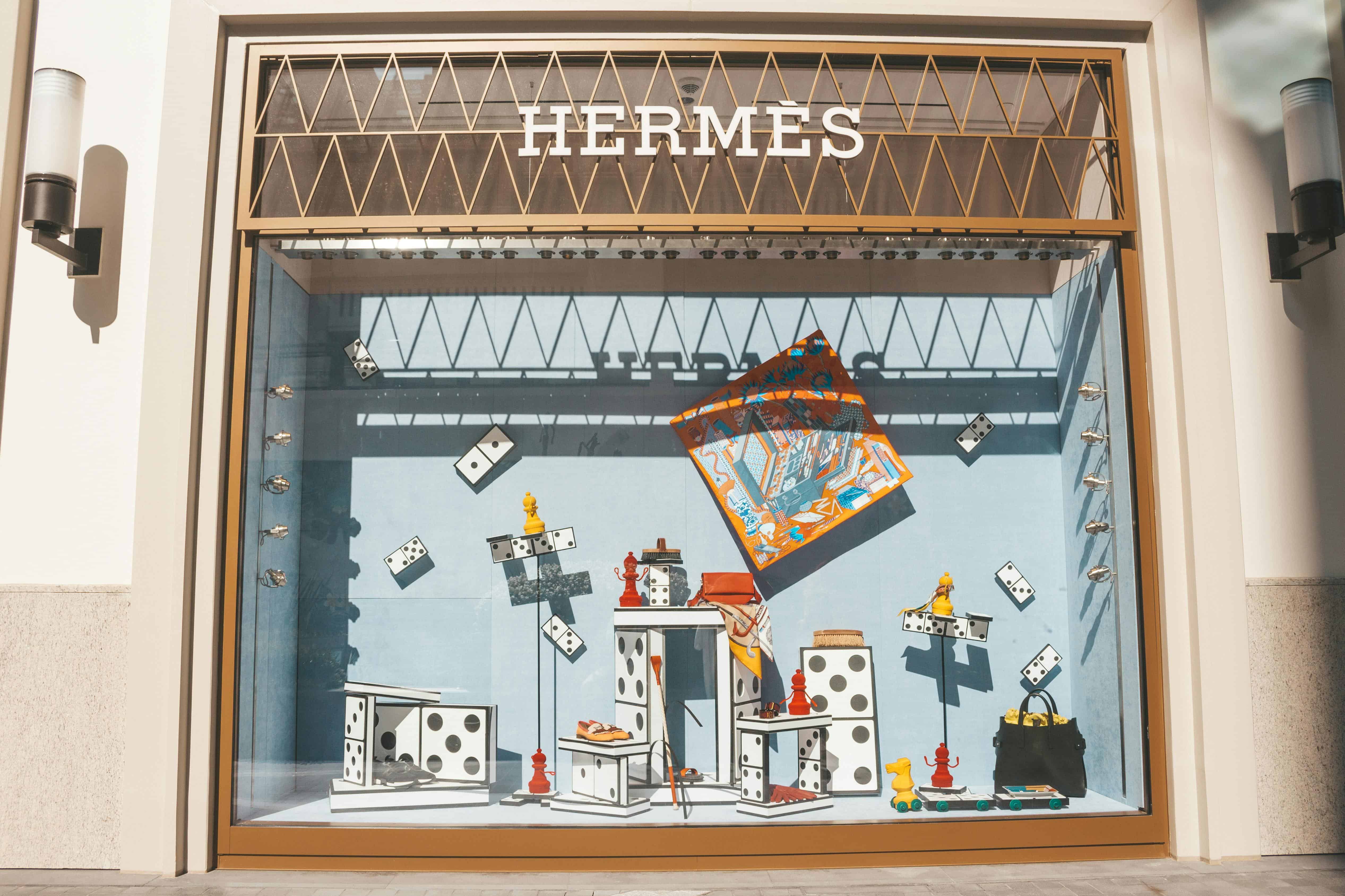 Luxury storefront display showing Hermes branding and high-end items arranged as visual symbols of status and consumption