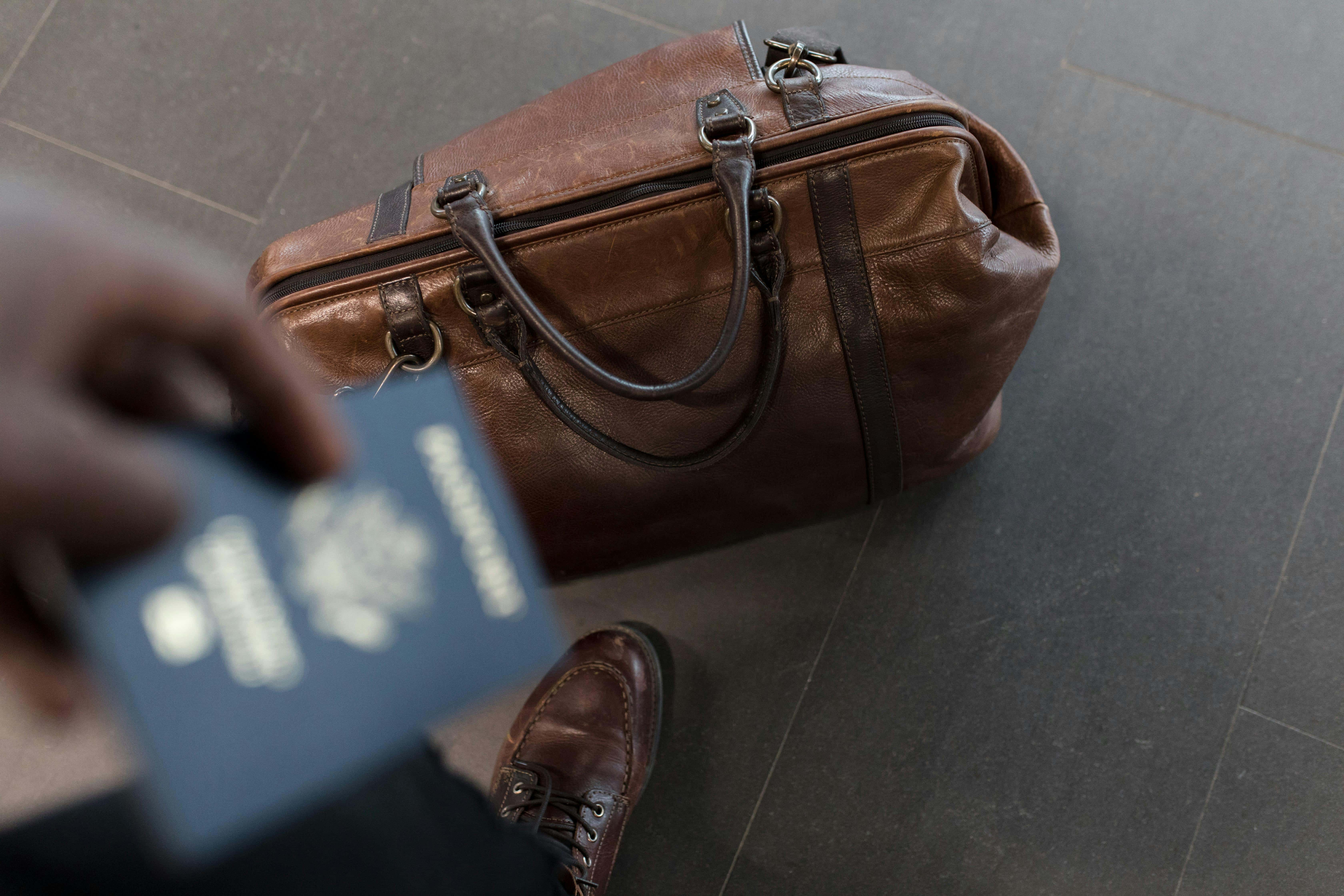 Traveler holding a passport beside a leather travel bag, representing international travel readiness and essential items you think you don’t need until something goes wrong